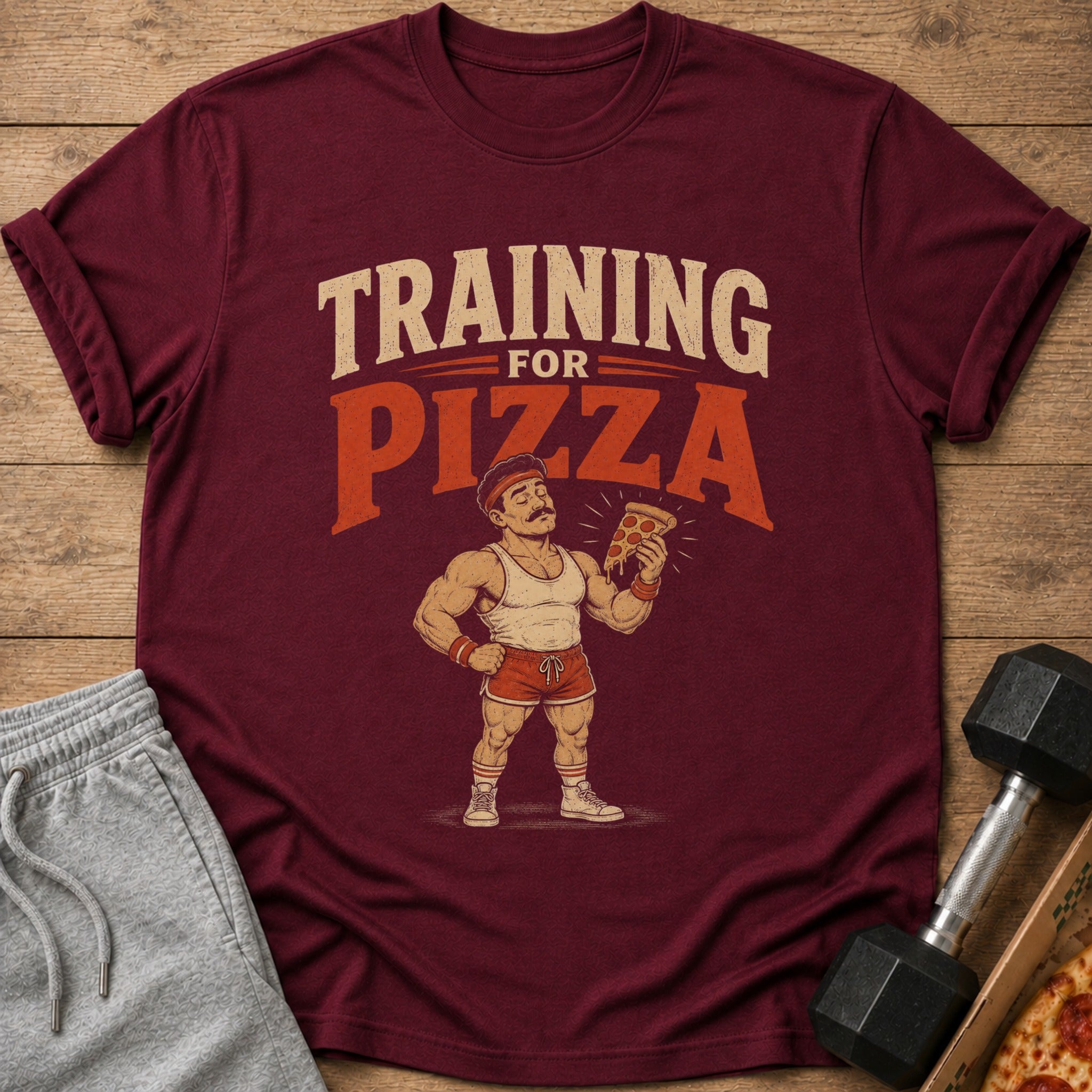 Maroon t-shirt with text "TRAINING FOR PIZZA" and illustration of muscular man holding pizza slice.