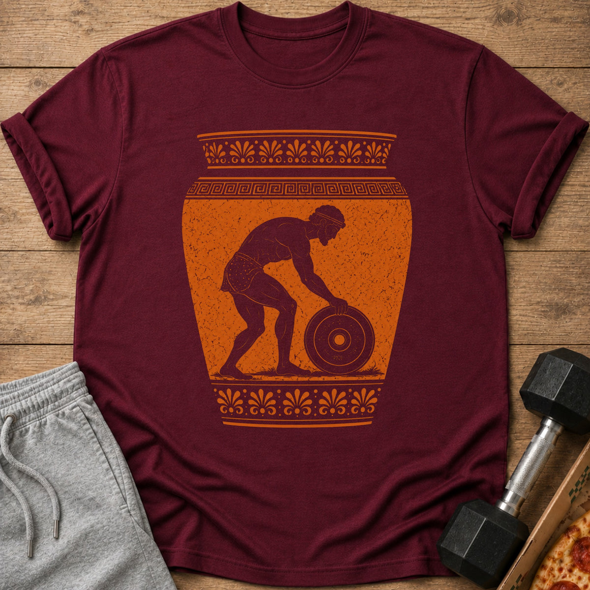 Maroon t-shirt with an ancient Greek style illustration of a man lifting a weight.