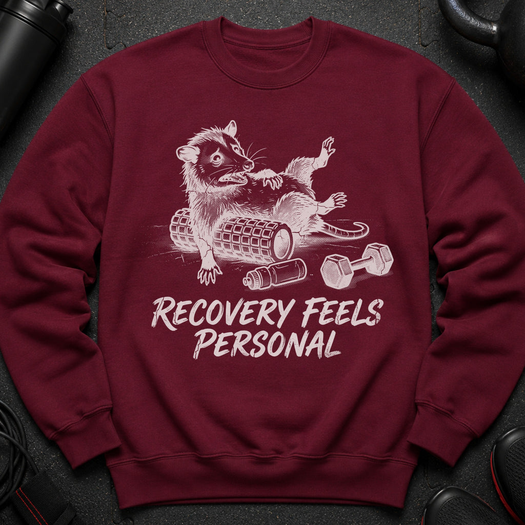 Maroon sweatshirt with graphic of a stylized raccoon on a foam roller, text "RECOVERY FEELS PERSONAL".