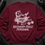 Maroon sweatshirt with graphic of a stylized raccoon on a foam roller, text "RECOVERY FEELS PERSONAL".