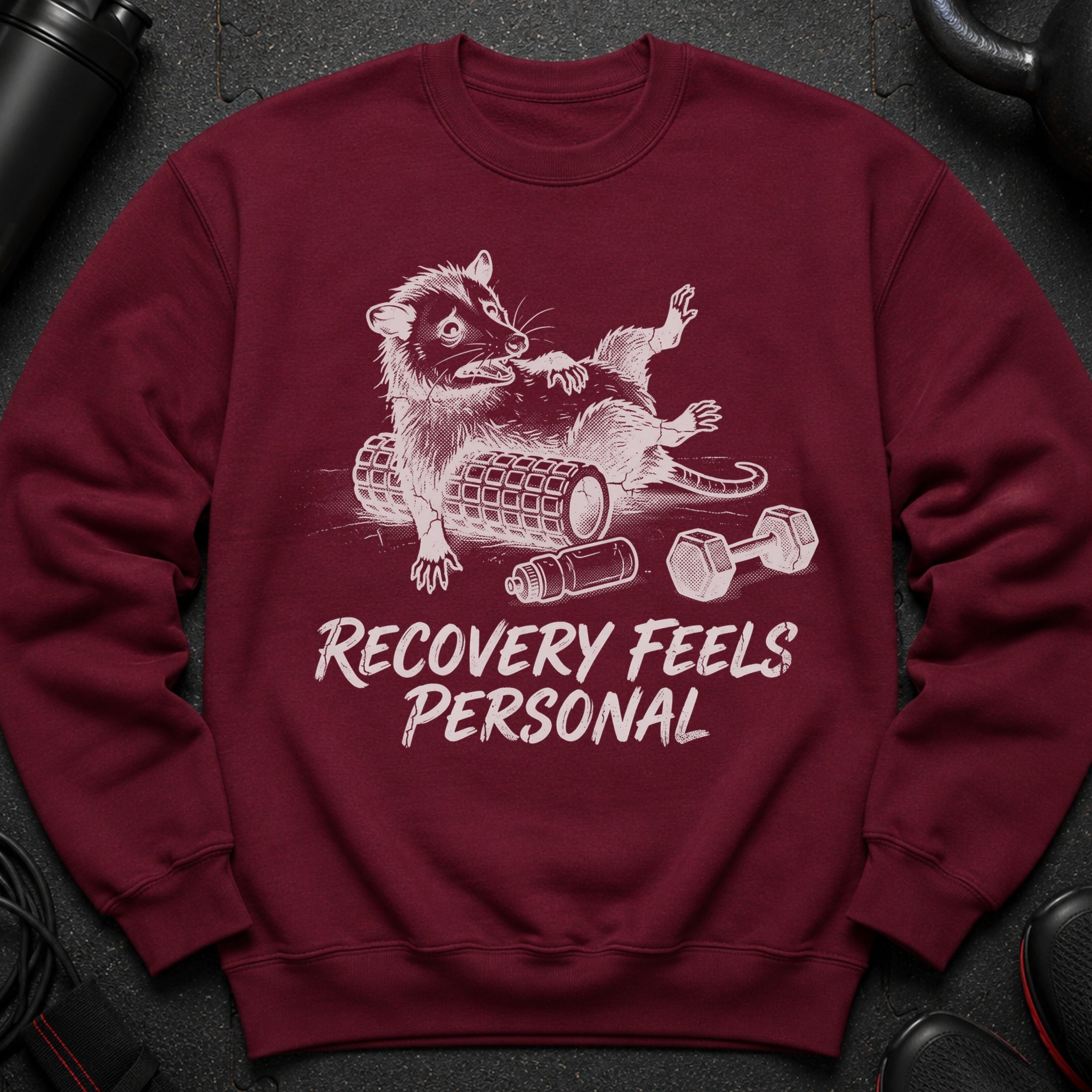 Maroon sweatshirt with graphic of a stylized raccoon on a foam roller, text "RECOVERY FEELS PERSONAL".