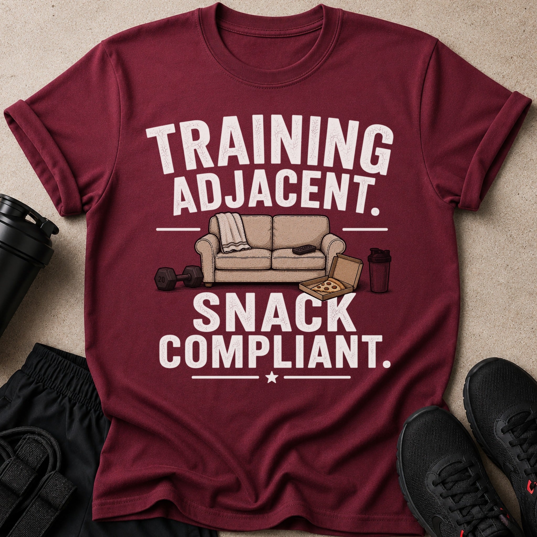 Maroon t-shirt with "TRAINING ADJACENT. SNACK COMPLIANT." text and gym accessories.