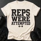 Light cream t-shirt with black distressed text "REPS WERE ATTEMPTED" and barbell graphic.