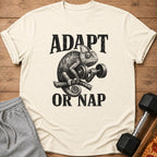 Chameleon lifting dumbbell with text "ADAPT OR NAP" on a cream t-shirt.