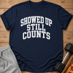 Navy t-shirt with white text "SHOWED UP STILL COUNTS" next to shorts and a dumbbell.