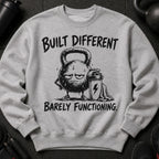 Gray sweatshirt with distressed illustration of a sweating kettlebell and text "BUILT DIFFERENT BARELY FUNCTIONING."