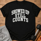 Black t-shirt with text "SHOWED UP STILL COUNTS" and athletic wear.