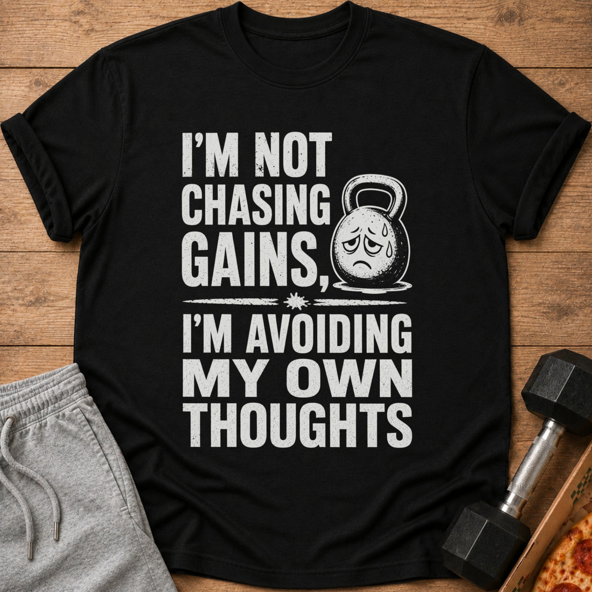 Black t-shirt with distressed text "I'm Not Chasing Gains, I'm Avoiding My Own Thoughts" and a sad kettlebell graphic.