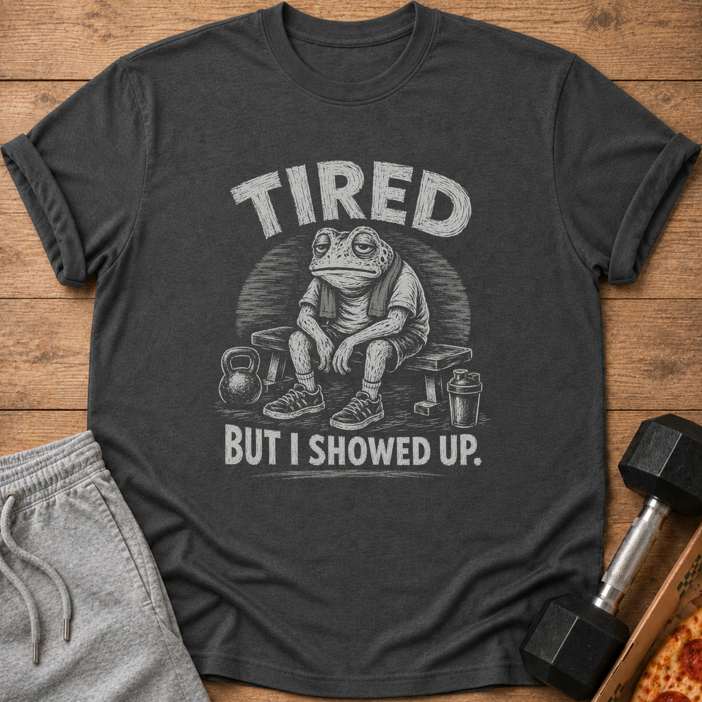 Dark grey t-shirt with a distressed graphic of a tired frog on a bench, with text "TIRED BUT I SHOWED UP."