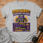 Grey t-shirt with pixel art graphic: "Side Quest: Survive Leg Day," a kettlebell character, and stats.